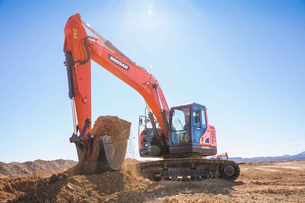 A powerful Doosan excavator moving dirt under a clear blue sky at a construction site.